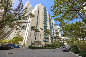 A high-rise residential building with multiple balconies, surrounded by palm trees and a clear sky.