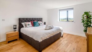 A bedroom with a large bed, a bedside table, a window, and a plant. - 2-bed Modern Bungalow - Outstanding Country Views (Harrogate)