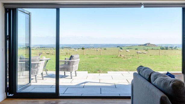 A modern living room with a large sliding glass door leading to a patio. - 2-bed Modern Bungalow - Outstanding Country Views (Harrogate)