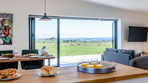 A modern dining area with a large table set for breakfast, a sofa, and a TV mounted on the wall. - 2-bed Modern Bungalow - Outstanding Country Views (Harrogate)