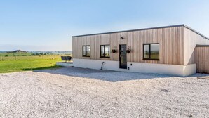 A modern building with a wooden exterior, a gravel driveway, and a view of the countryside. - 2-bed Modern Bungalow - Outstanding Country Views (Harrogate)