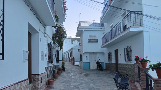 A narrow cobblestone street flanked by white buildings with balconies, potted plants, and a parked motorcycle. - Impeccable 1-bed House in Sayalonga (Sayalonga)