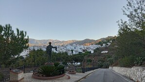 A statue on a stone pedestal in a landscaped area with a road in the foreground and a town in the background. - Impeccable 1-bed House in Sayalonga (Sayalonga)