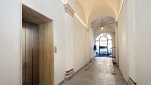 A hallway with a herringbone-patterned floor, a wooden elevator door, and an arched window at the end.