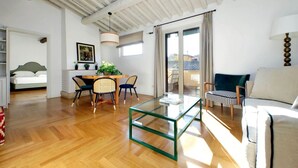 A spacious living area with a wooden floor, a glass coffee table, a sofa, and a dining table with chairs.