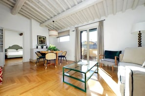 A spacious living area with a wooden floor, a glass coffee table, a sofa, and a dining area with chairs and a table.