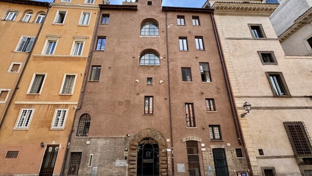 A multi-story building with a central arched entrance, multiple windows, and a stone facade.