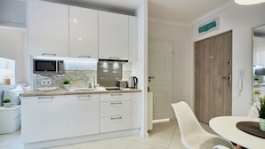 Une cuisine moderne avec des meubles blancs, un four à micro-ondes, une bouilloire et un évier. Il y a également un coin repas avec une table et des chaises blanches.