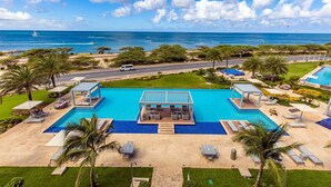 A resort with a large swimming pool, lounge areas, and a view of the ocean. - Discover Ocean View Condo Living (Oranjestad)