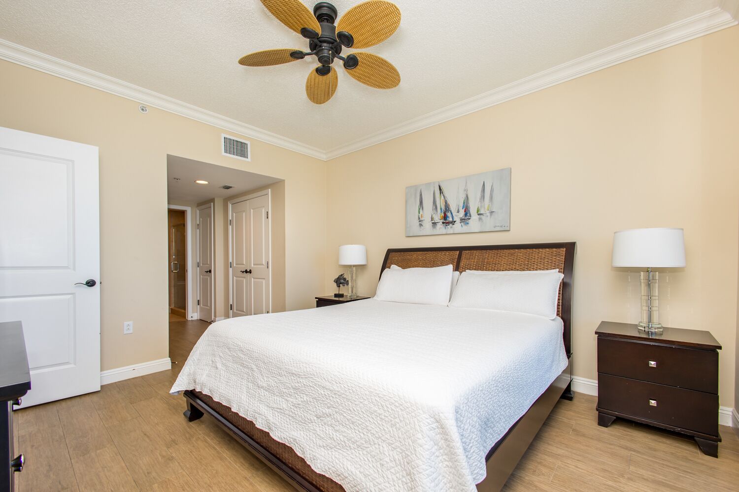 Sink into crisp white linens beneath a coastal ceiling fan, where warm tones and thoughtful details create your tranquil retreat after sun-soaked days.