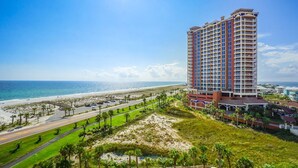 Un hotel moderno con vista al mar, varios balcones y una zona bien cuidada con palmeras y una carretera.