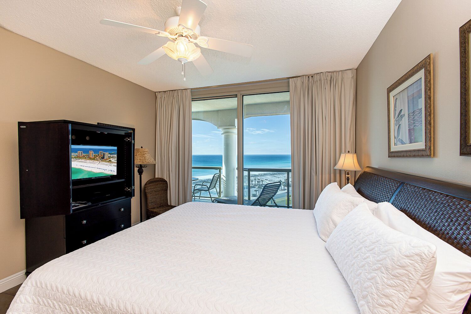 Une chambre d’hôtel avec un grand lit, une télévision, un ventilateur de plafond et un balcon avec vue sur l’océan.