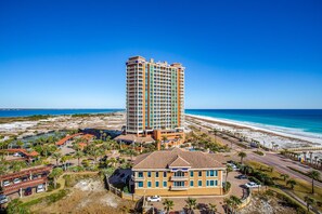 A high-rise hotel with a beach view, featuring multiple balconies and a parking area with palm trees. - P1-1008 Seas the Day -Gulf Front Portofino! (Pensacola Beach)