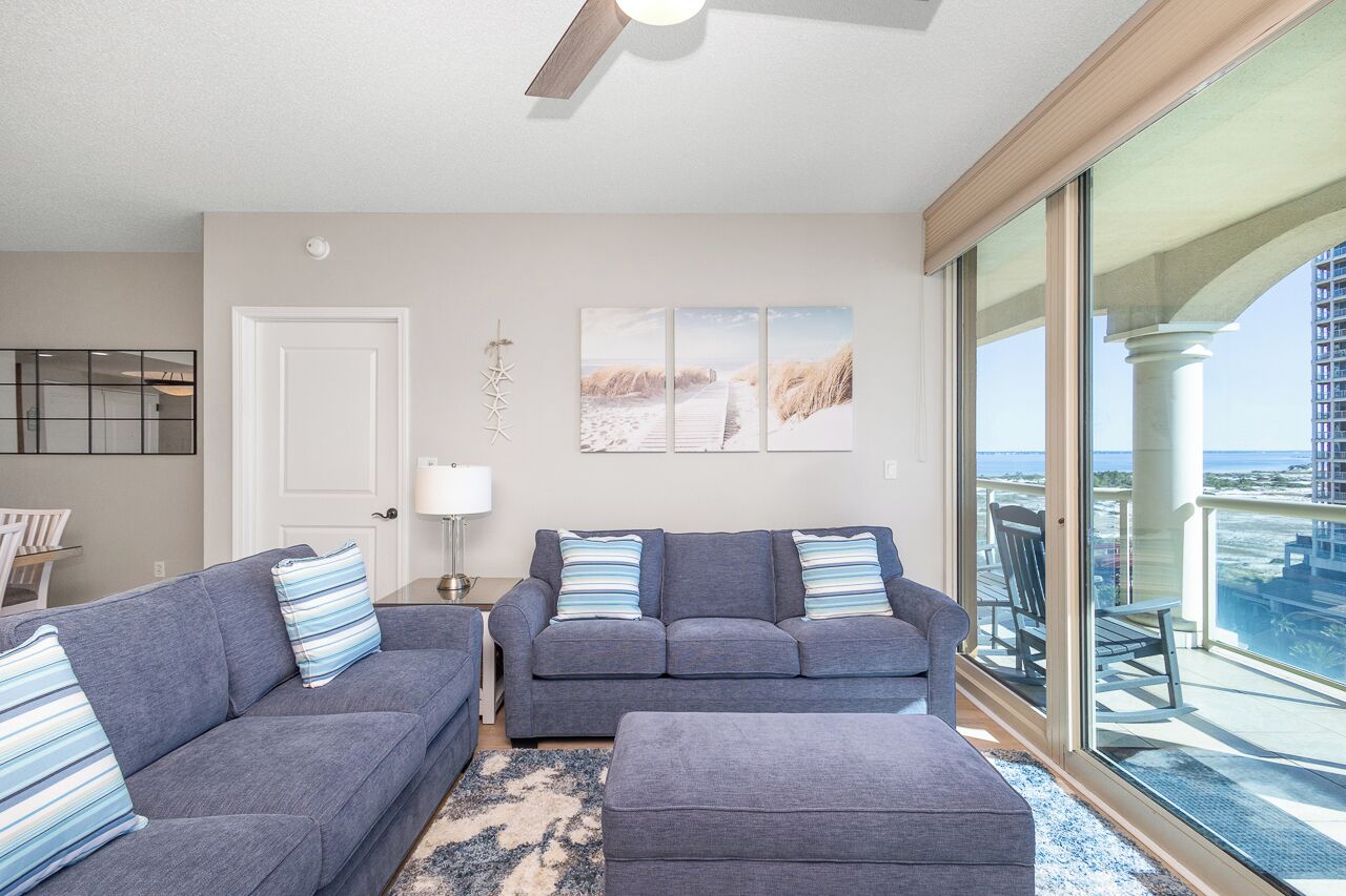 A living room with two grey sofas, a small table, and a large window with a balcony.