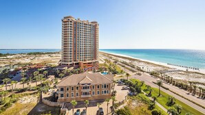 Ein Hochhotel mit Blick auf den Strand, ein Parkplatz und ein kleineres Gebäude mit einem Balkon.