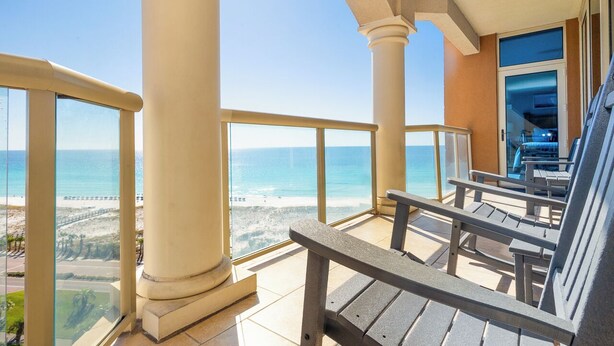 Ein Balkon mit Meerblick, Holzstühle und eine Glastür zum Poolbereich.