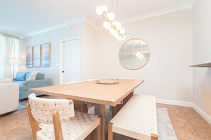 A dining area with a wooden table, woven chairs, a round mirror, and a hanging light fixture.