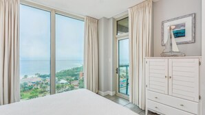 A bedroom with a large bed, a wardrobe, and a view of a coastal area. - P1-1105 2B Island View @ Portofino (Pensacola Beach)