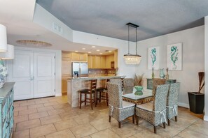 A spacious kitchen with modern appliances, a dining area with wicker chairs, and a chandelier.