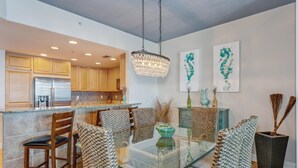A modern kitchen with wooden cabinets, a stainless steel refrigerator, and a glass dining table with woven chairs. - P1-1606 2B Condo @Portofino/ Steps from the Beach! (Pensacola Beach)