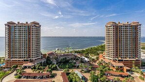 A high-rise hotel with a view of the ocean, featuring multiple floors, a parking area, and a landscaped courtyard. - P1-1606 2B Condo @Portofino/ Steps from the Beach! (Pensacola Beach)