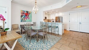 A spacious dining area with a glass table and metal chairs, a patterned rug, and a modern kitchen in the background. - 2B Island View @Portofino -Sleeps 7 in P1-1805 (Pensacola Beach)
