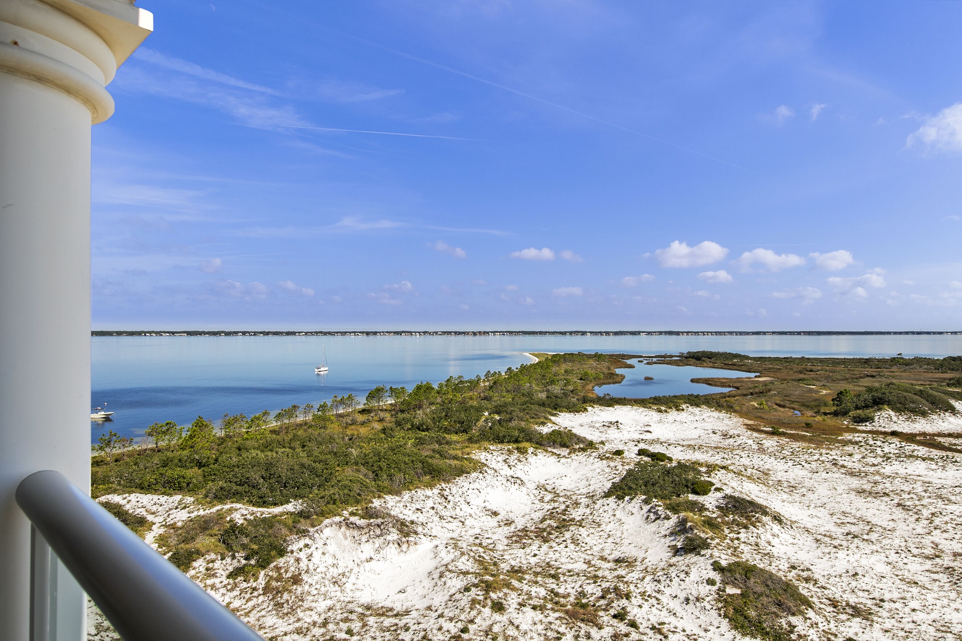 A coastal landscape with a bridge in the distance, sandy terrain, and sparse vegetation.