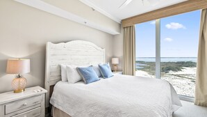 Une chambre avec un grand lit, une table de chevet avec une lampe et une vue sur la plage.