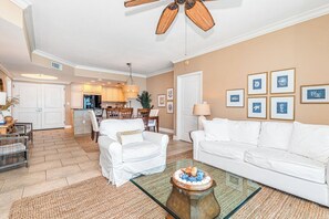A spacious living room with a glass coffee table, white sofas, and a ceiling fan.