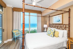 A room with a four-poster bed, a view of the ocean, a chair, and a lamp.