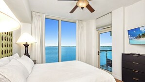 Un dormitorio con una cama grande, un ventilador de techo, un televisor y vistas al océano.