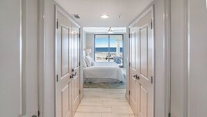 A hallway leading to a bedroom with a bed, a nightstand, and a view of the beach. - 2B Gulf Front w Private Terrace/Tower 3! (Pensacola Beach)
