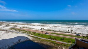 Een kustweg met uitzicht op het strand, een heldere lucht en enkele auto's op de weg.