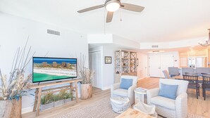 A modern living room with a flat-screen TV, wooden furniture, and a ceiling fan. - Stunning Gulf Front Views*Tower 3-0709 (Pensacola Beach)
