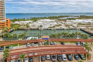 A multi-story hotel with a tennis court and parking area.