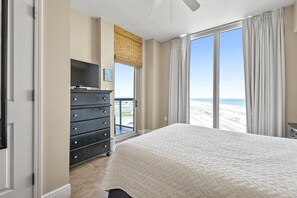 Une chambre dotée d’un grand lit, d’une commode, d’un téléviseur et offrant une vue sur la plage grâce à une porte-fenêtre coulissante.