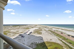 A view from a balcony overlooking a beach with a parking lot and a road.