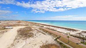 Eine Küstenstraße führt zu einem Strand, der von blauem Himmel und vereinzelten Wolken gesäumt ist.
