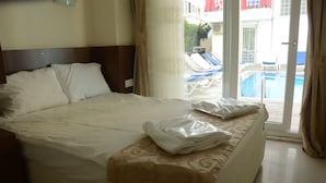 A hotel room with a bed, a window with a view of a pool and lounge chairs, and a door to the pool area. - Honor A Pansiyon Side (Manavgat)