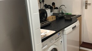 Een compacte keuken met een ingebouwde wasmachine, een magnetron en houten kastjes.