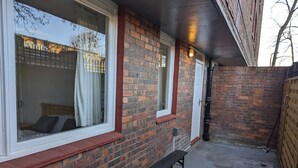 Een bakstenen gebouw met een overdekte patio, een bankje en een raam met uitzicht op een woonwijk.