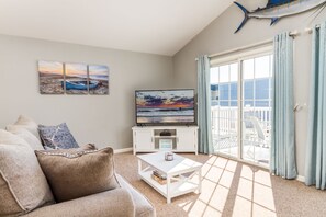 Relax in this stylish living room with a comfortable sofa, flat-screen TV, and sliding glass door leading to a scenic outdoor area.