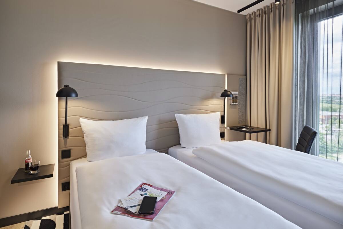 Habitación de hotel con dos camas, una mesita de noche con una botella de Coca-Cola, un vaso y una revista.