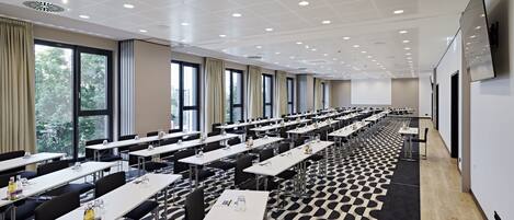 Une salle de conférence équipée de plusieurs tables, de chaises et d’un écran de projection.