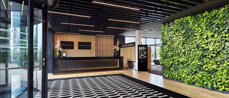 A modern hotel lobby with a reception desk, a patterned carpet, and a green wall.