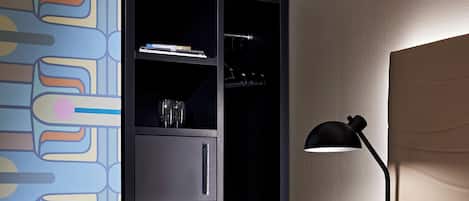 Une chambre d’hôtel comprenant un lit, une lampe de chevet, une armoire avec des étagères et un mur orné d’un motif abstrait aux couleurs vives.