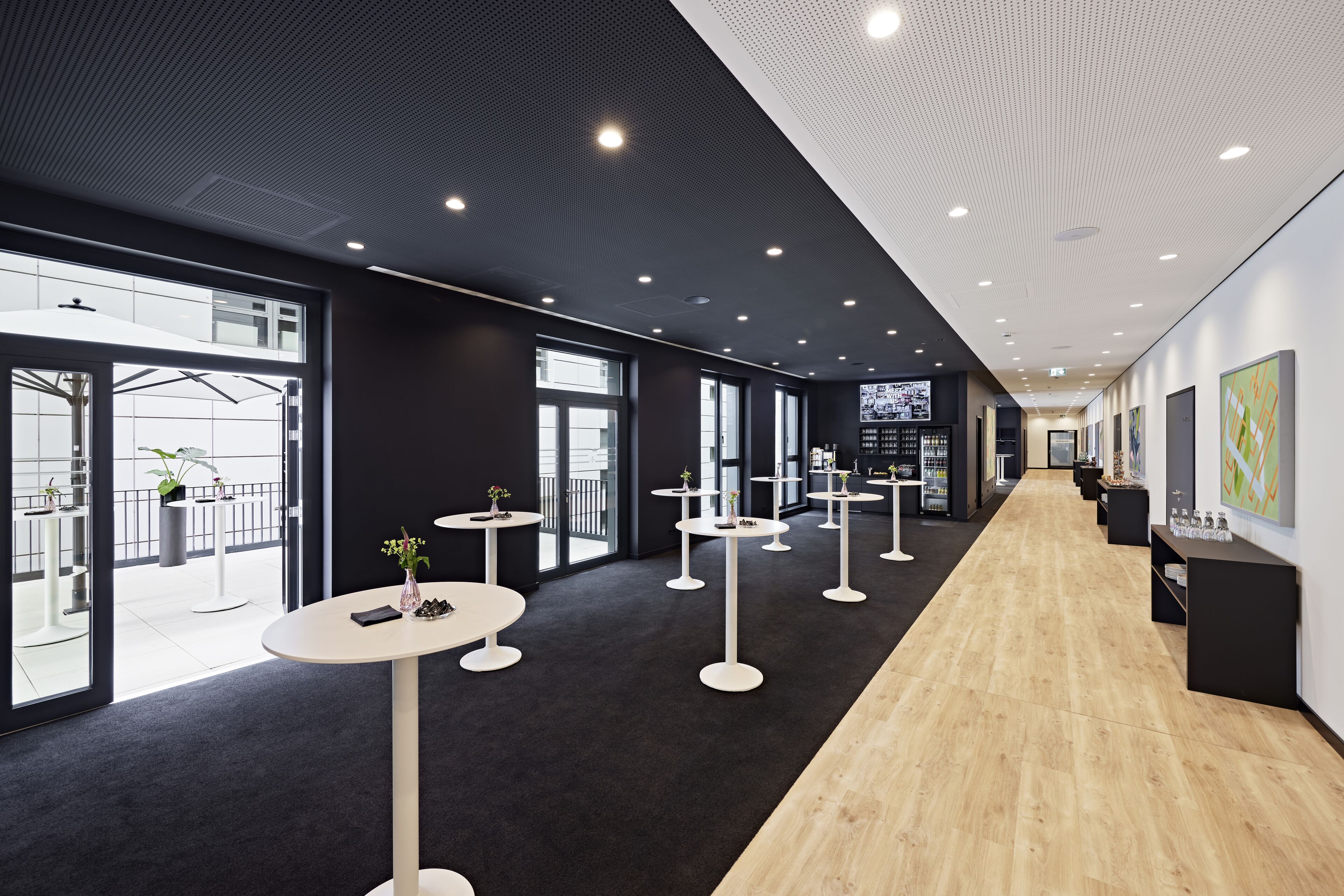 En moderne hotellobby med en central gang, runde borde og en kombination af naturligt og kunstigt lys.