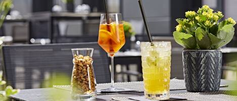 A table with drinks and a small plant, set against a modern building facade.