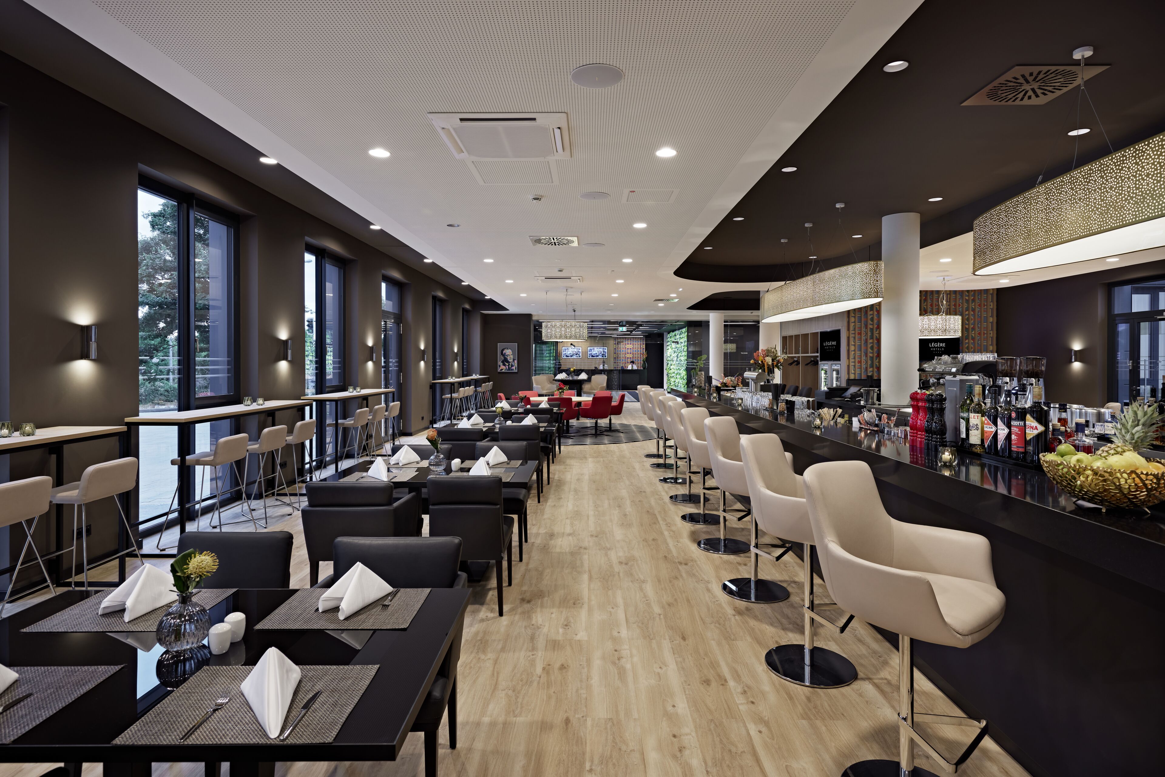 A modern restaurant with a long counter, multiple tables, and chairs.