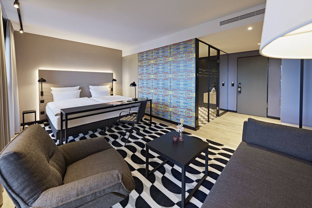 Una habitación de hotel moderna con una cama, un escritorio, un sofá y una alfombra estampada.